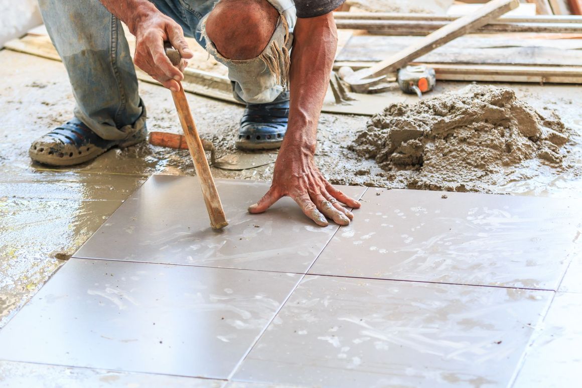 Man laying floor tiles, using a tool. Cement and building materials are present.
