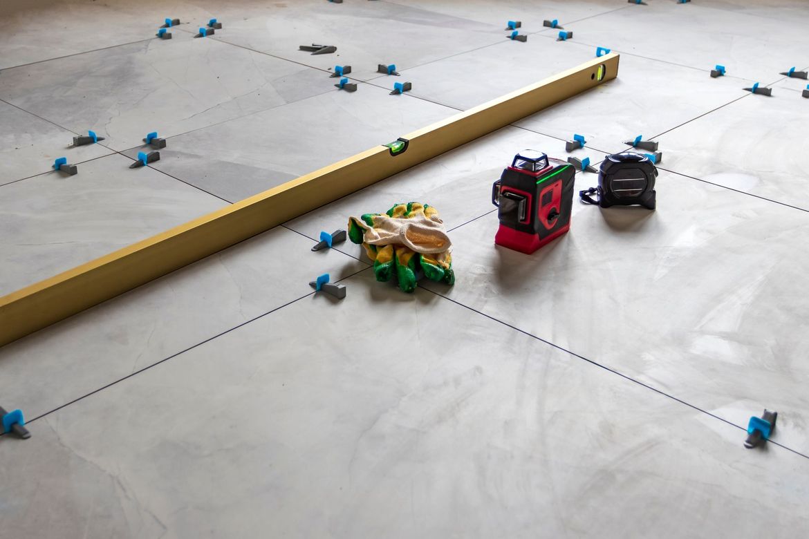 Level and tools on a floor marked with lines, ready for tiling.