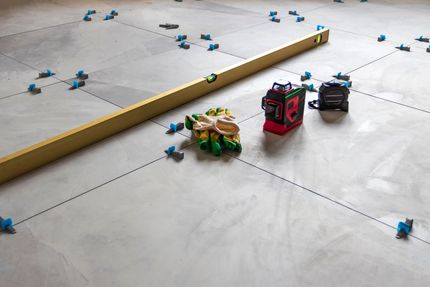 Level and tools on a floor marked with lines, ready for tiling.