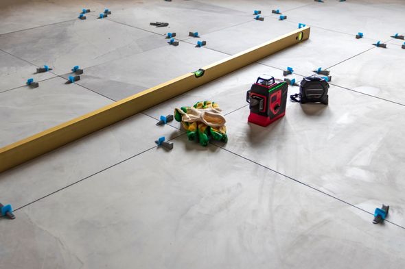 Level and tools on a floor marked with lines, ready for tiling.