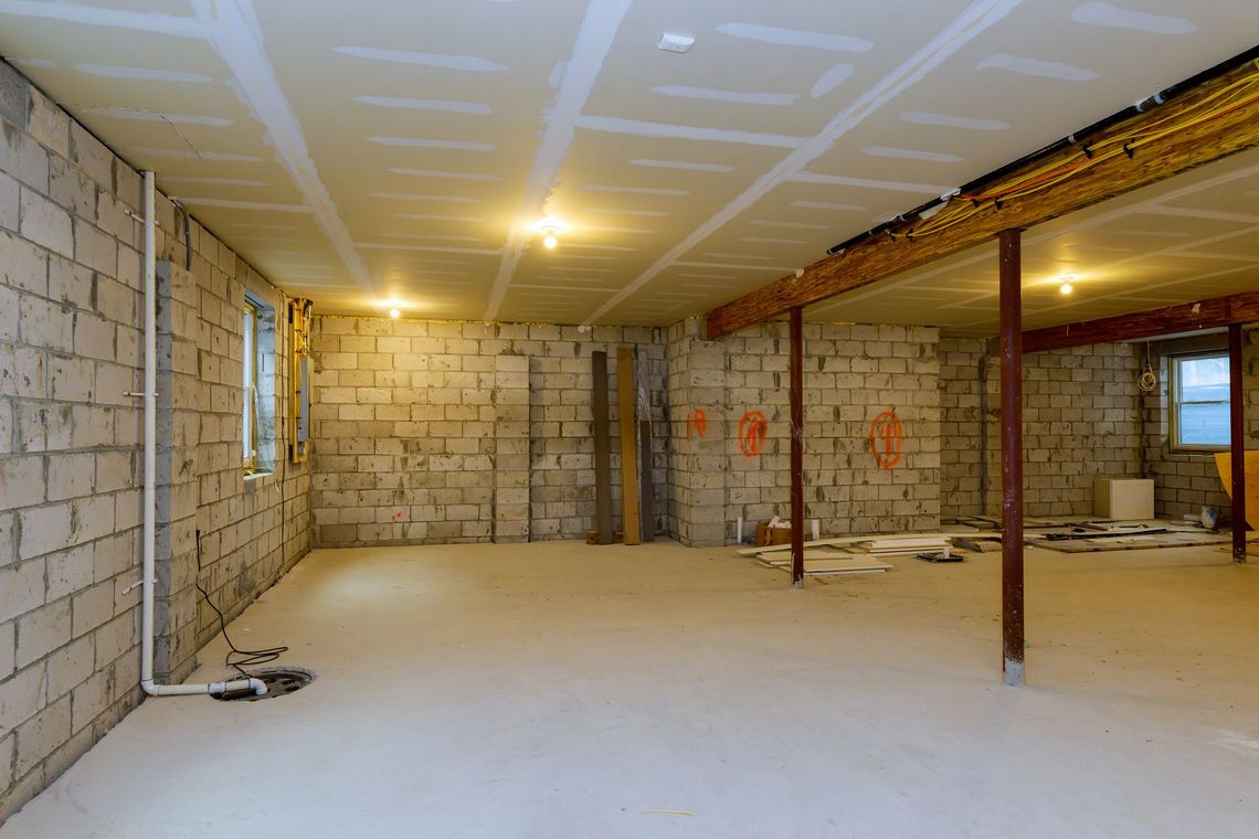 Basement under construction, exposed cinder block walls, drywall ceiling, concrete floor, overhead lighting.