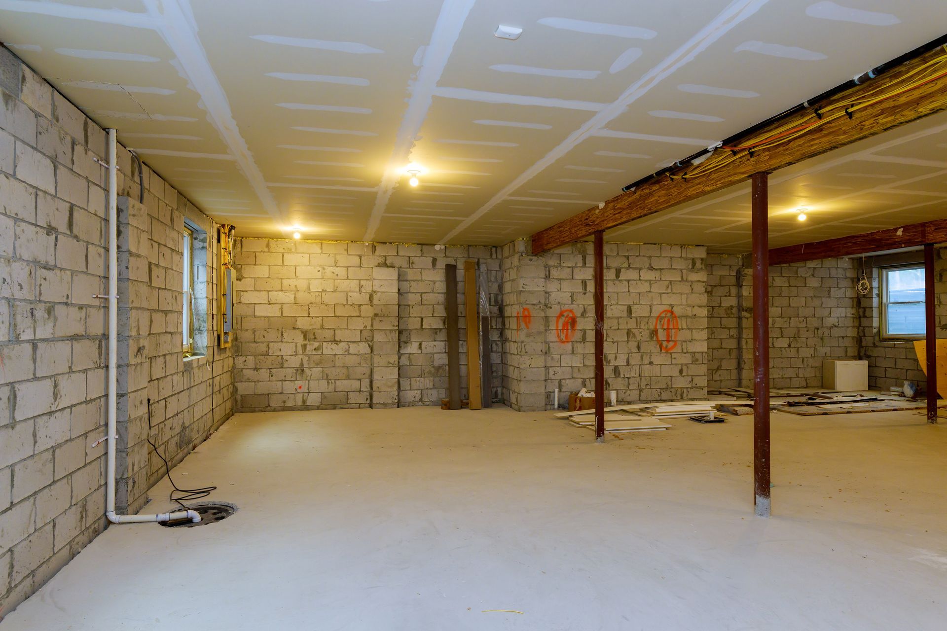 Basement under construction, exposed cinder block walls, drywall ceiling, concrete floor, overhead lighting.