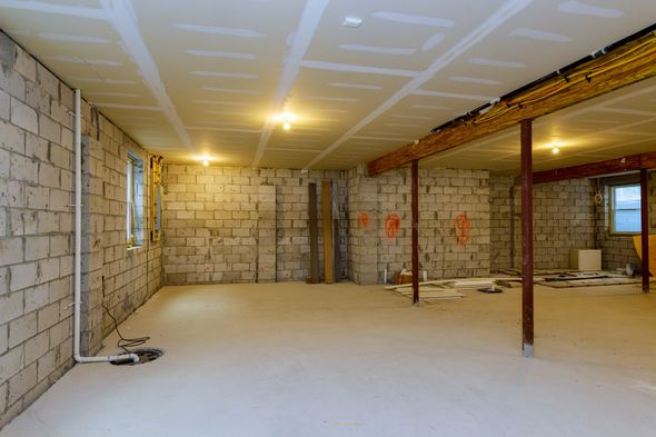 Basement under construction, exposed cinder block walls, drywall ceiling, concrete floor, overhead lighting.