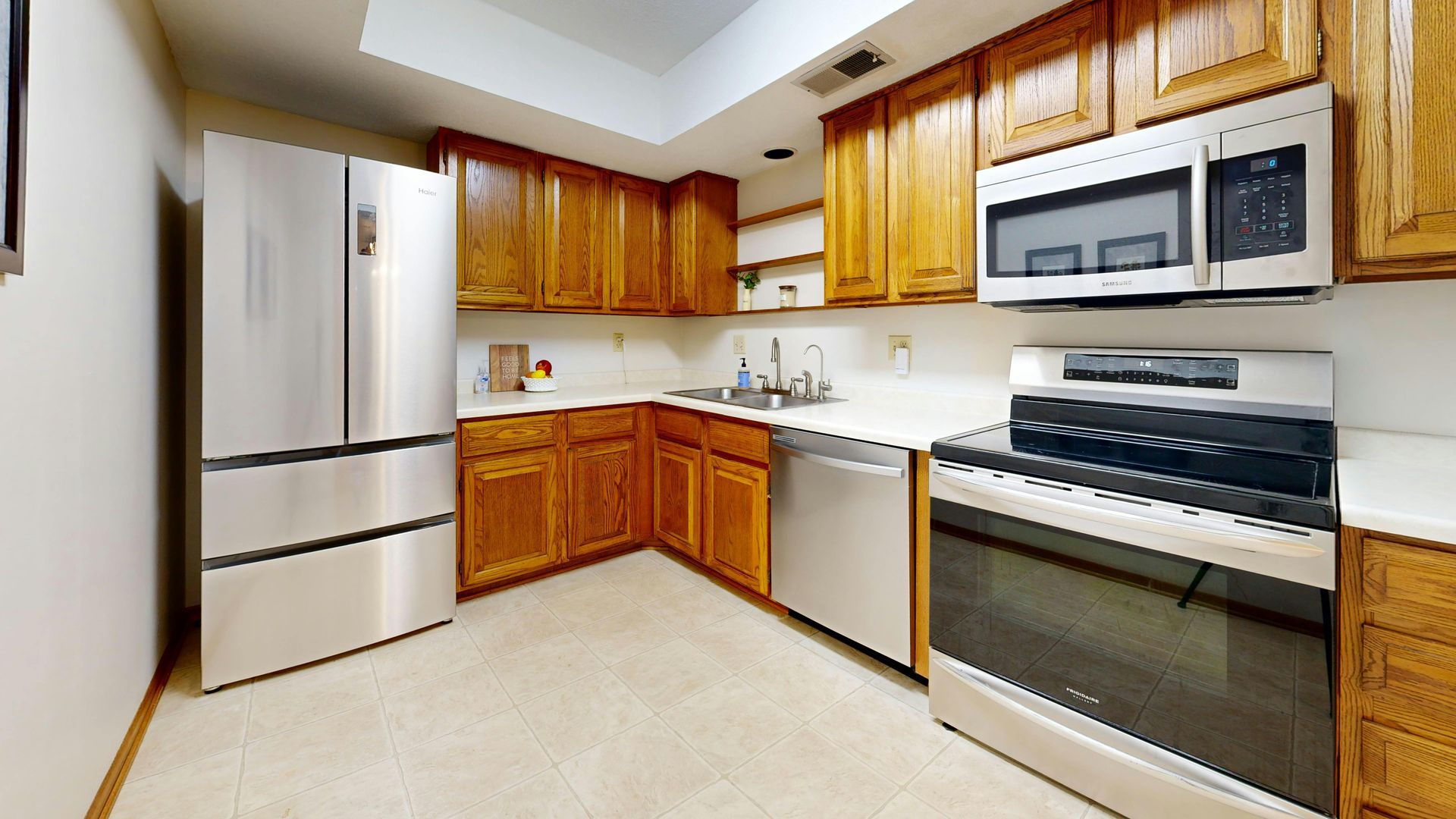 A modern U-shaped kitchen with oak cabinets, stainless steel appliances, and tile flooring.