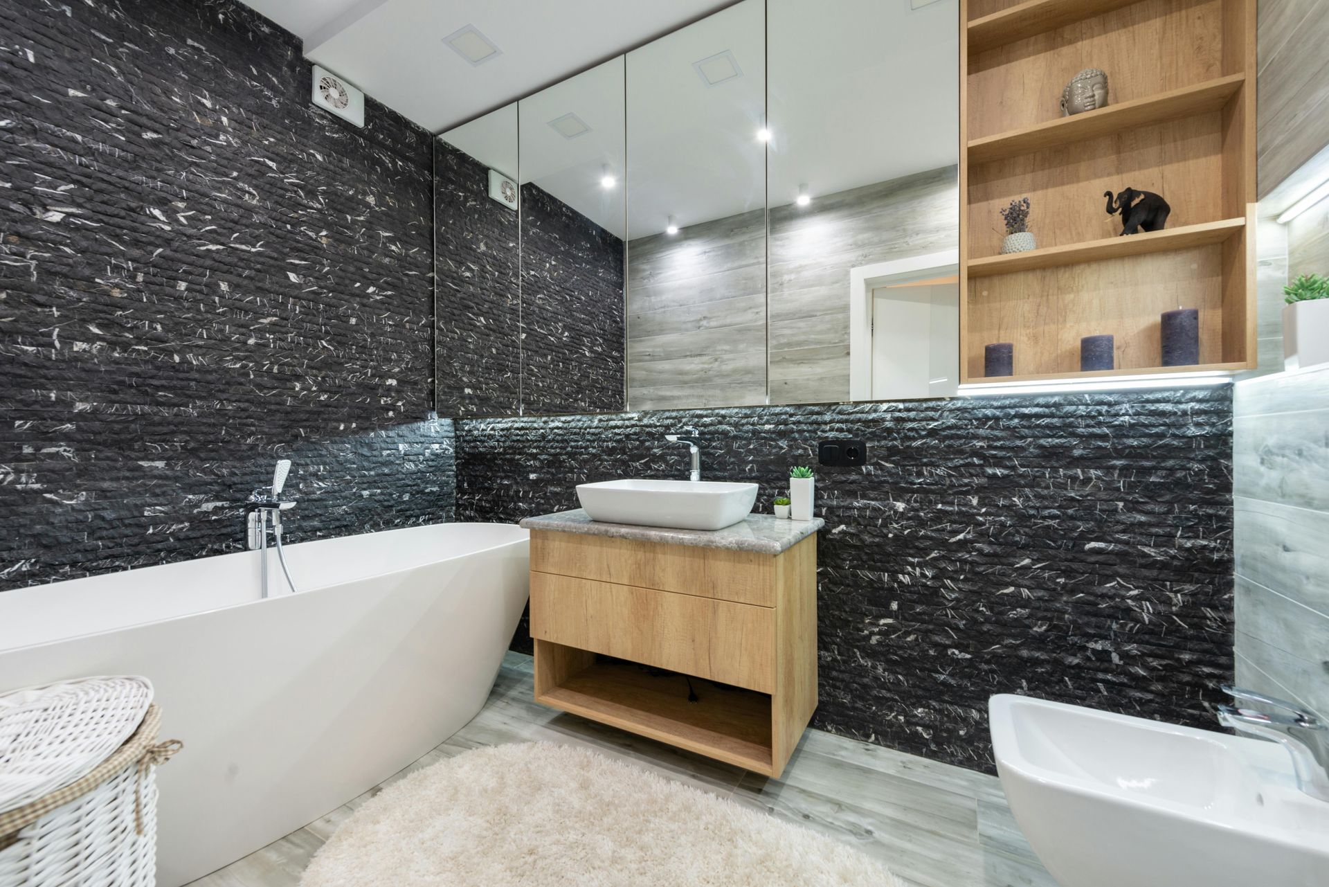 Modern bathroom with black marble walls, white tub and sink, wood vanity, and mirror cabinet