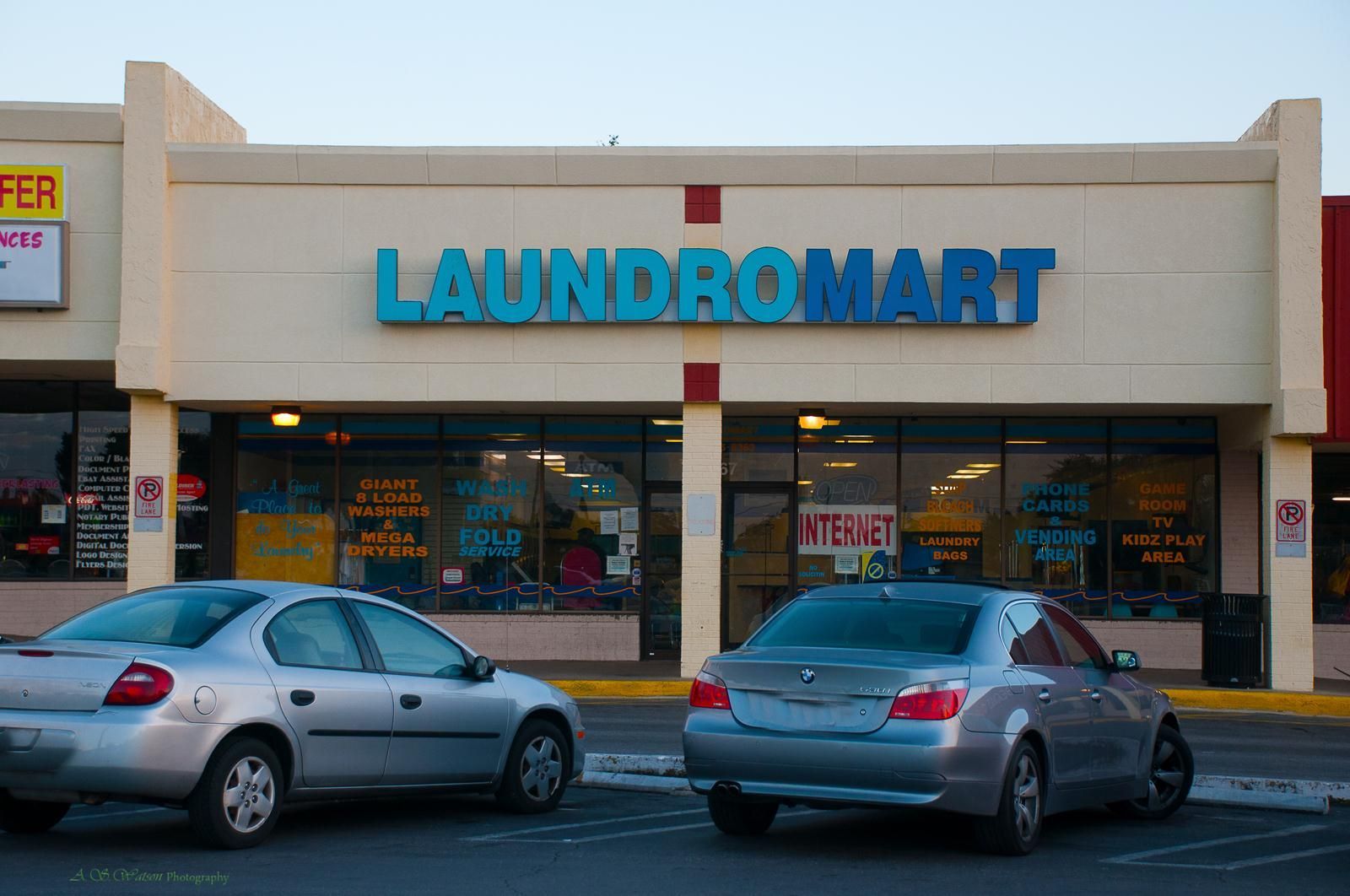 Two silver cars are parked in front of a tan commercial building with a blue 