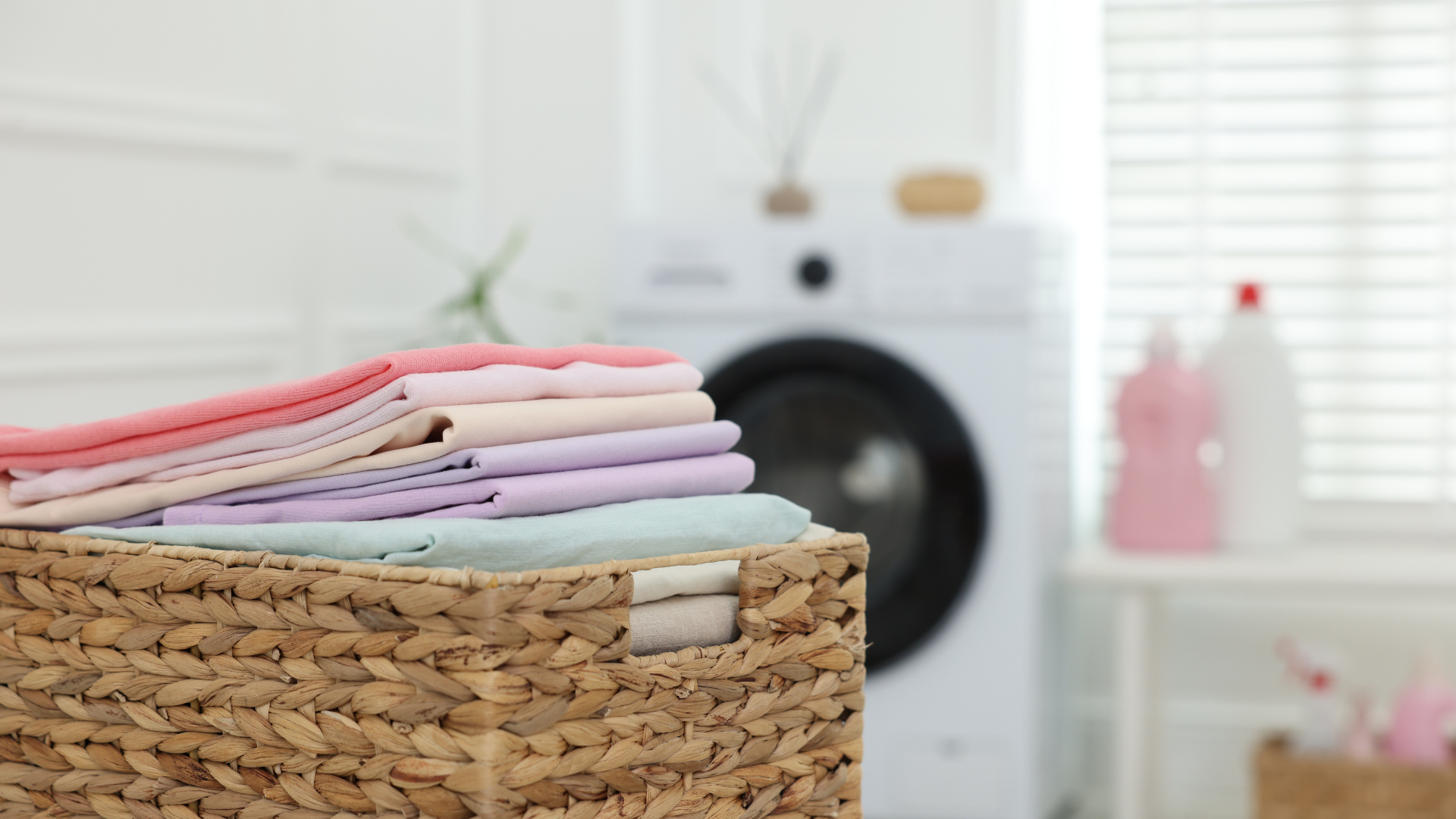 A wicker basket filled with neatly folded pastel-colored laundry sits in front of a white washing machine.