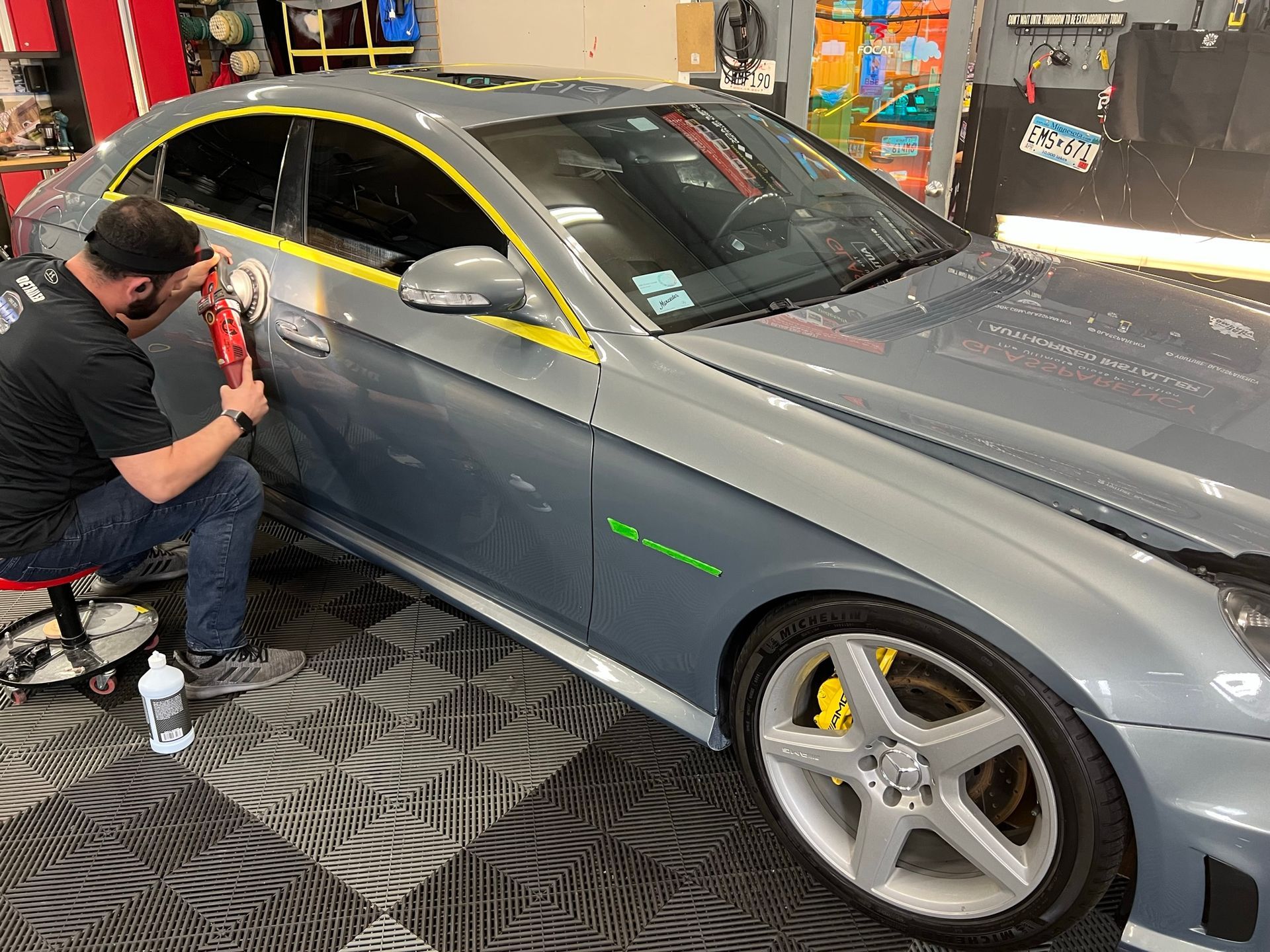 Man polishing a gray Mercedes-Benz car in a garage. The car has yellow brake calipers and a green logo.