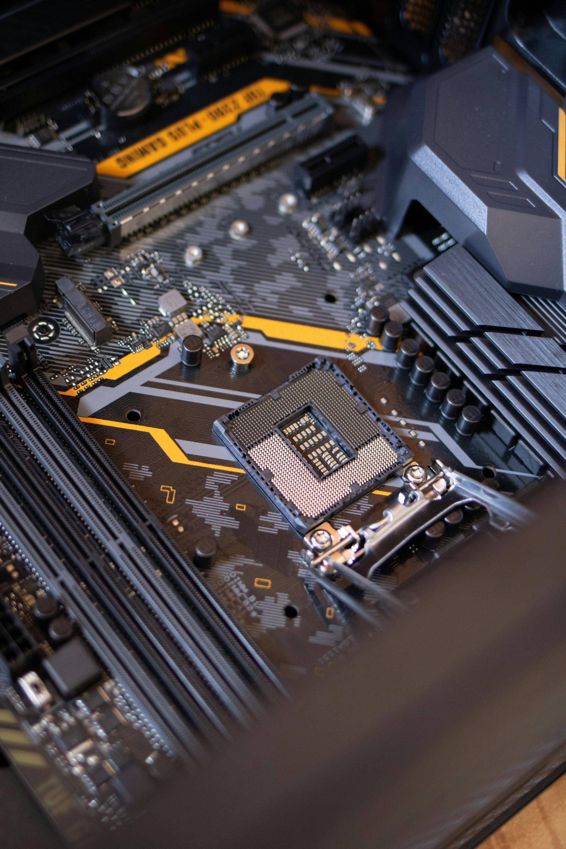 A close-up of a computer motherboard with an empty CPU socket, yellow accents, and black components.