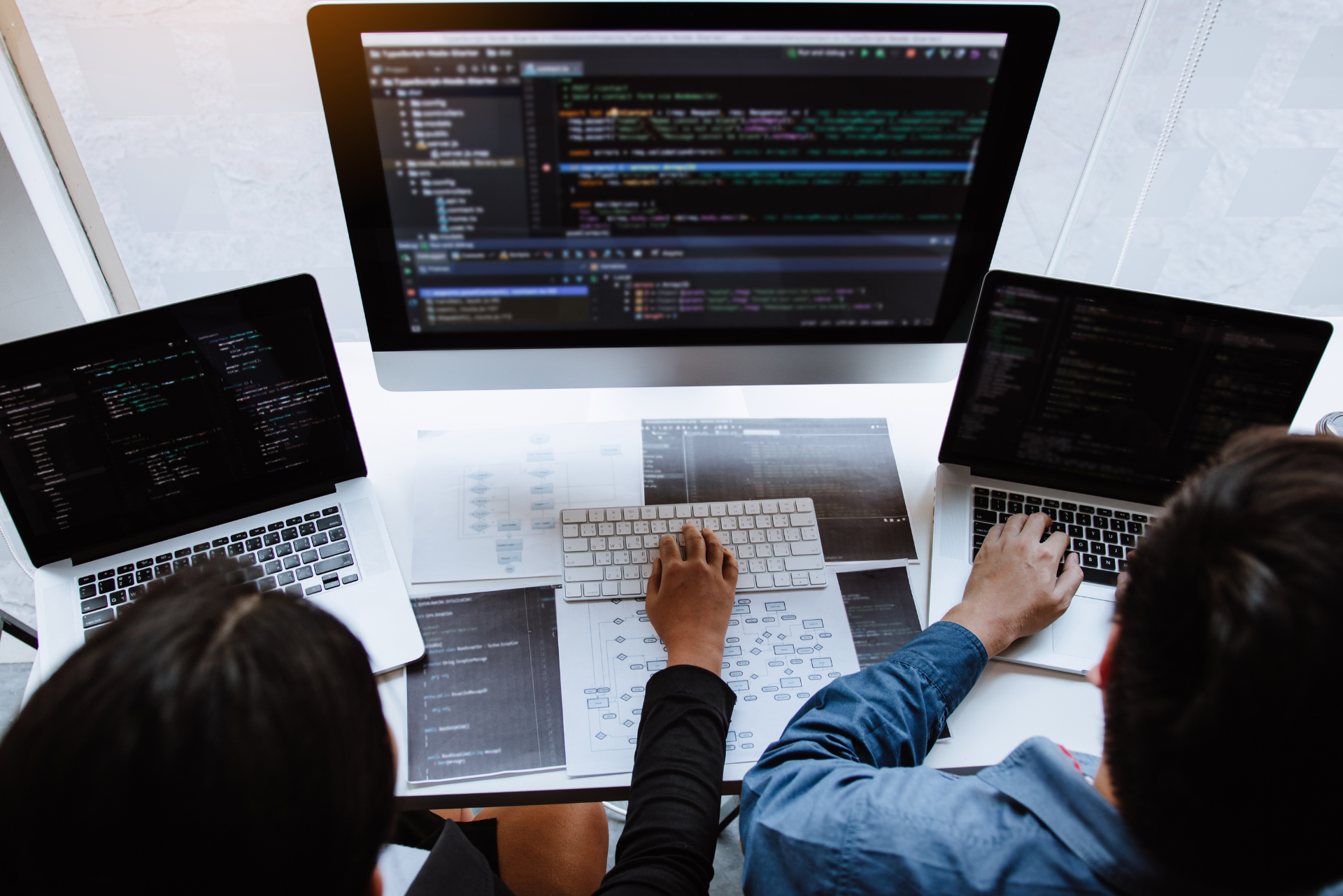 Un grupo de personas está sentada en una mesa usando computadoras y laptops.