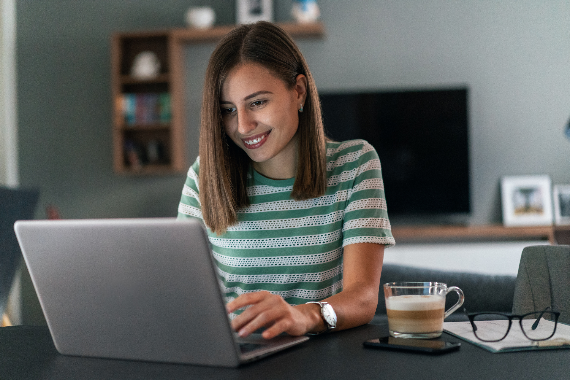 Una mujer está sentada en una mesa usando una computadora portátil.