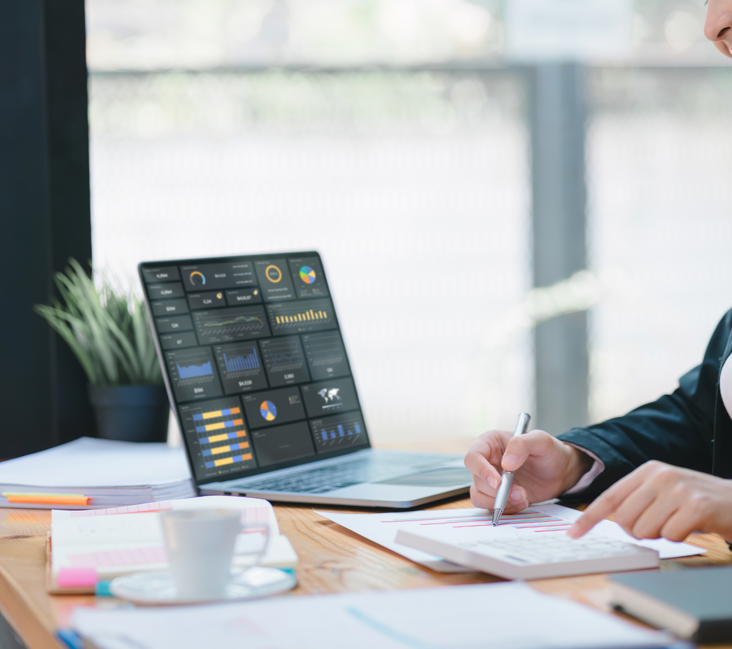 Una mujer está sentada en un escritorio con una computadora portátil y una taza de café.