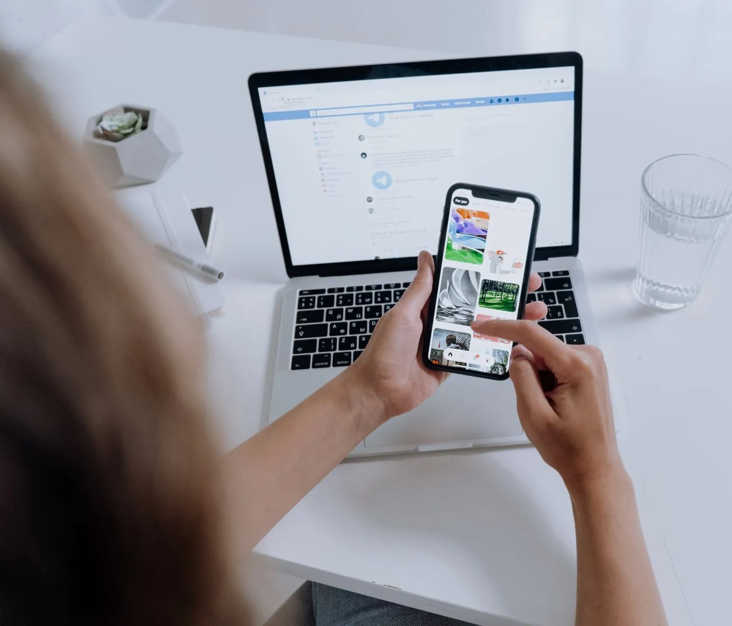 Una persona está sentada en un escritorio usando una computadora portátil y un teléfono celular.