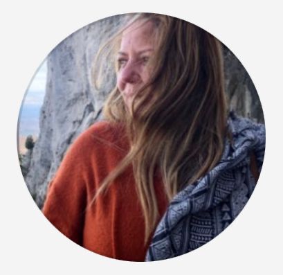 Uma mulher com um suéter laranja está parada em frente a uma parede de pedra