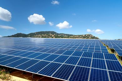 Solar panels stretching across a coastal landscape under a bright blue sky with clouds