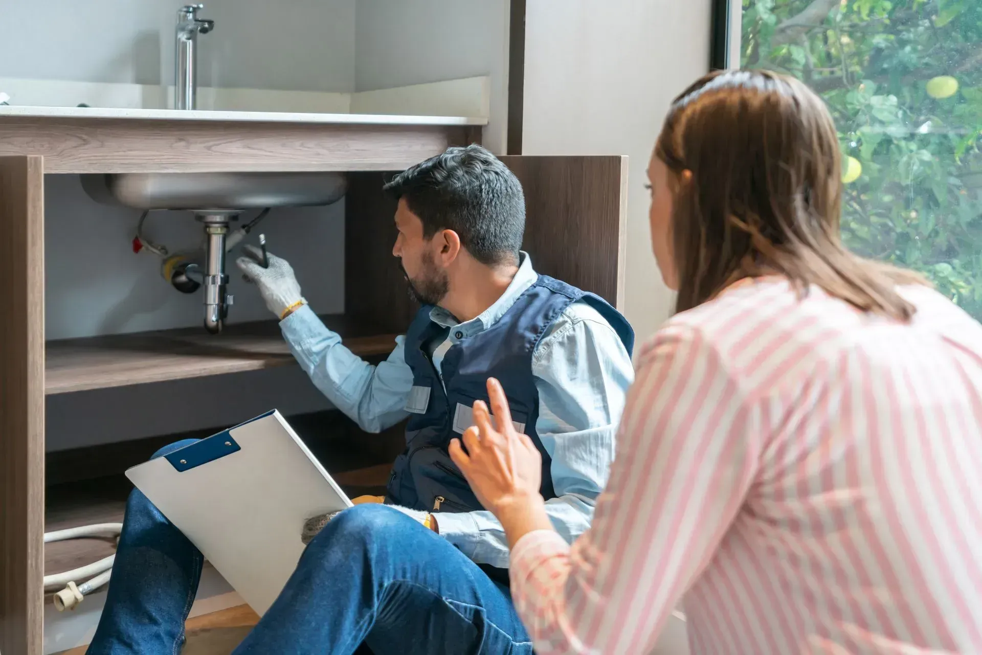 A man is fixing a sink while a woman looks on.
