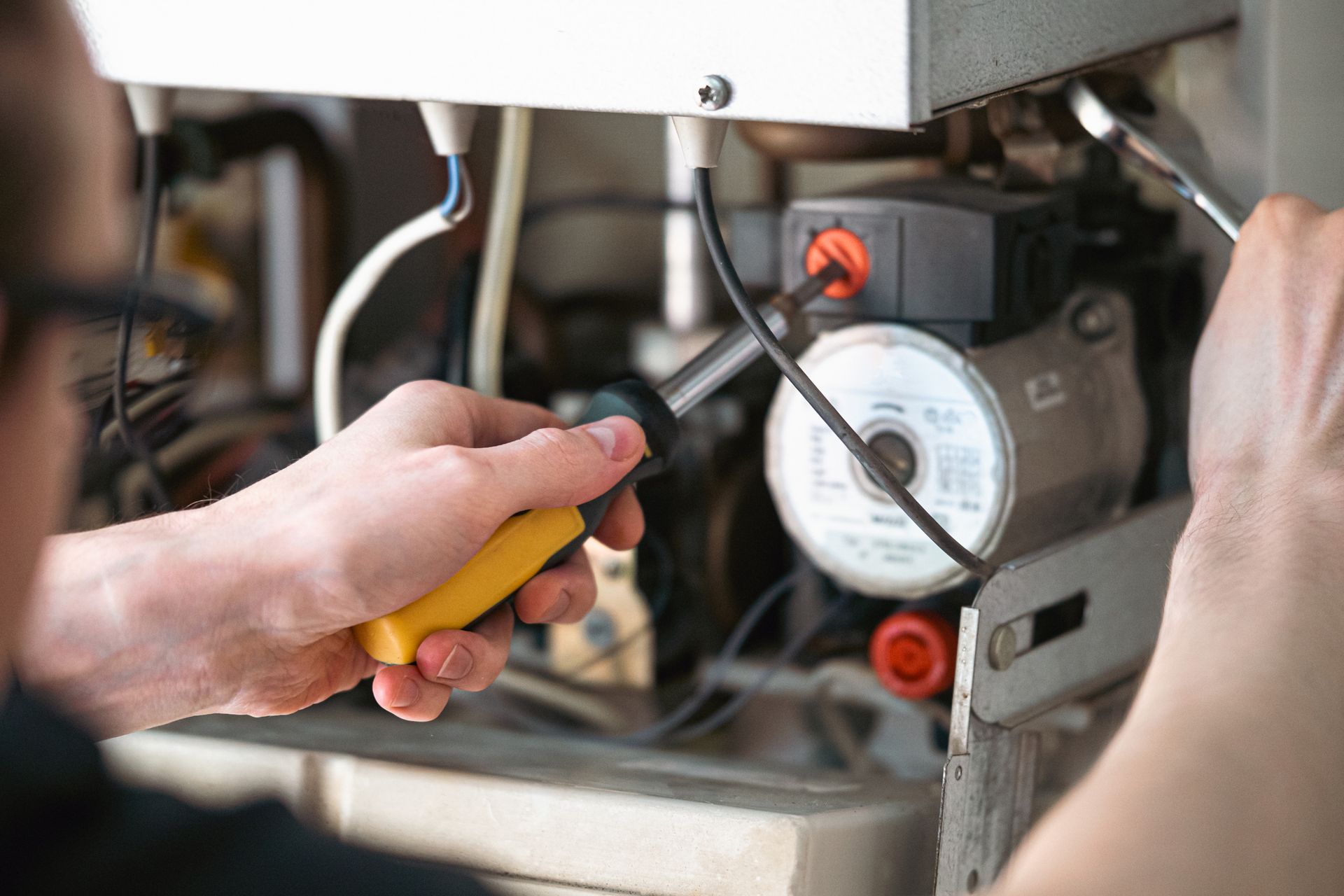 A man is fixing a boiler with a screwdriver.