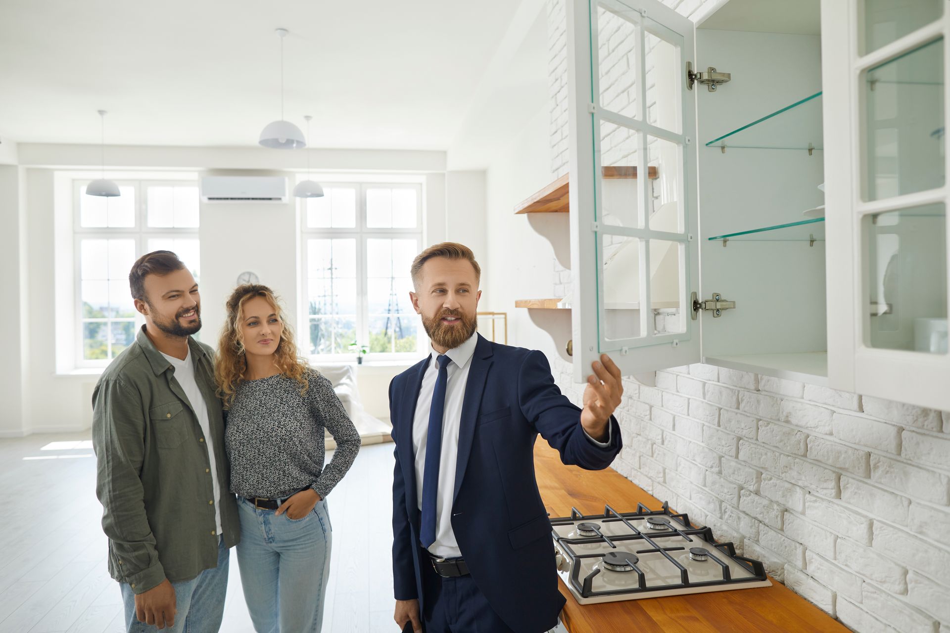A professional agent showing a couple a real estate rental kitchen with a white brick backsplash.