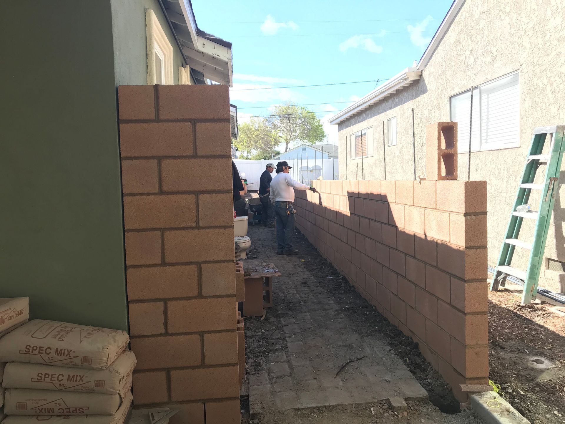 A bricklayer aligns bricks using a yellow leveling string on a wall under construction.