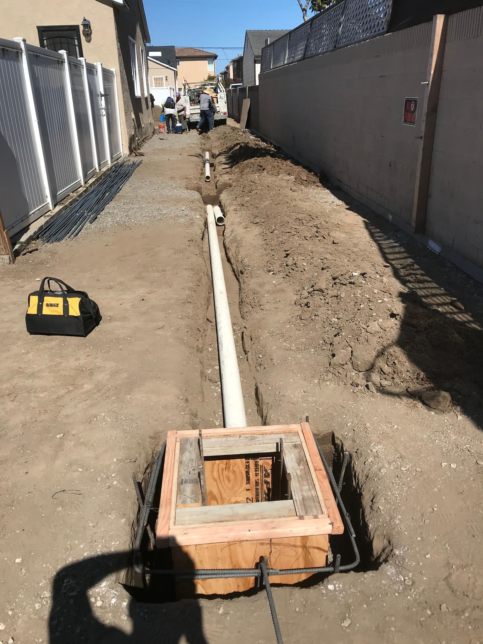 Black plastic irrigation pipes with blue couplings installed in a narrow dirt trench.