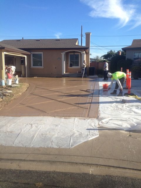 A newly installed red stamped concrete driveway leading to a garage, with wooden formwork still along the edges.