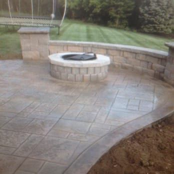 A freshly poured concrete patio in a backyard setting, showing smooth, wet gray surfaces divided by control joints.
