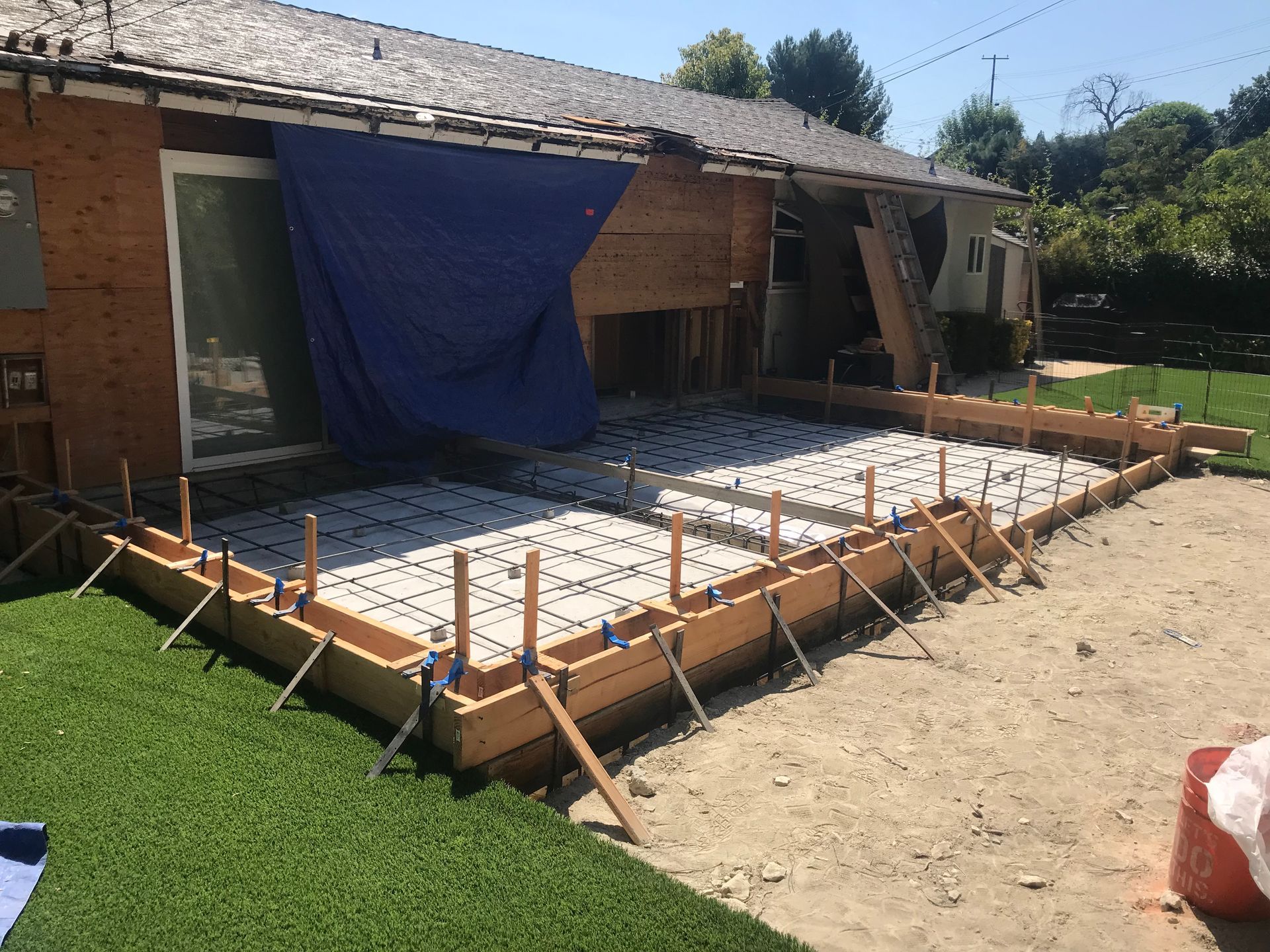 A concrete foundation for a new house under construction, with wooden framing visible in the background.