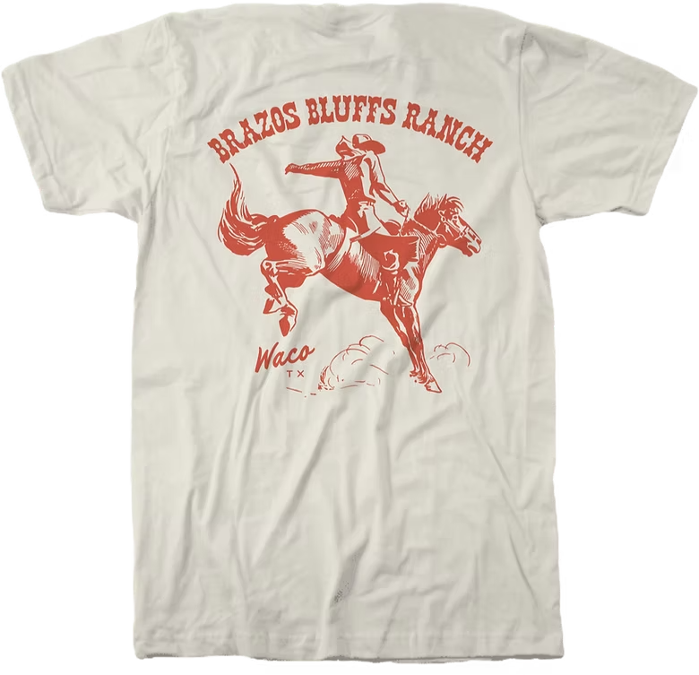 Cream-colored t-shirt with orange graphic of a cowboy on a bucking horse; text reads 