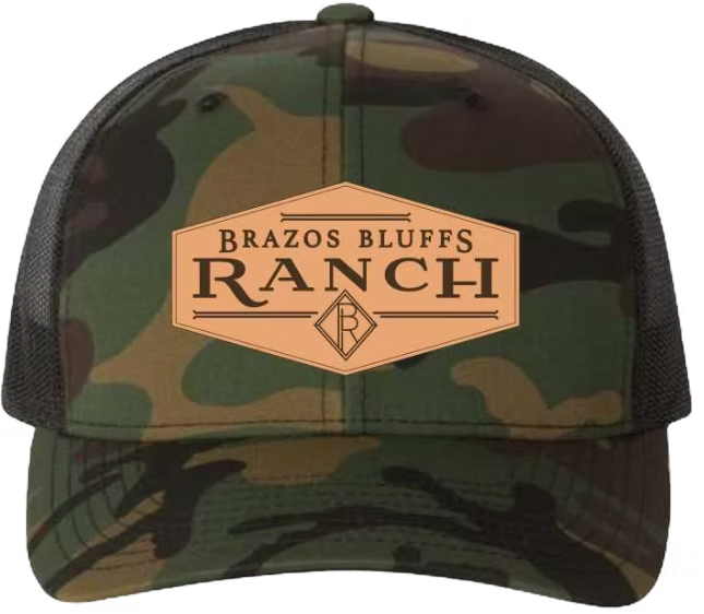 Camouflage trucker hat with a tan leather patch reading 