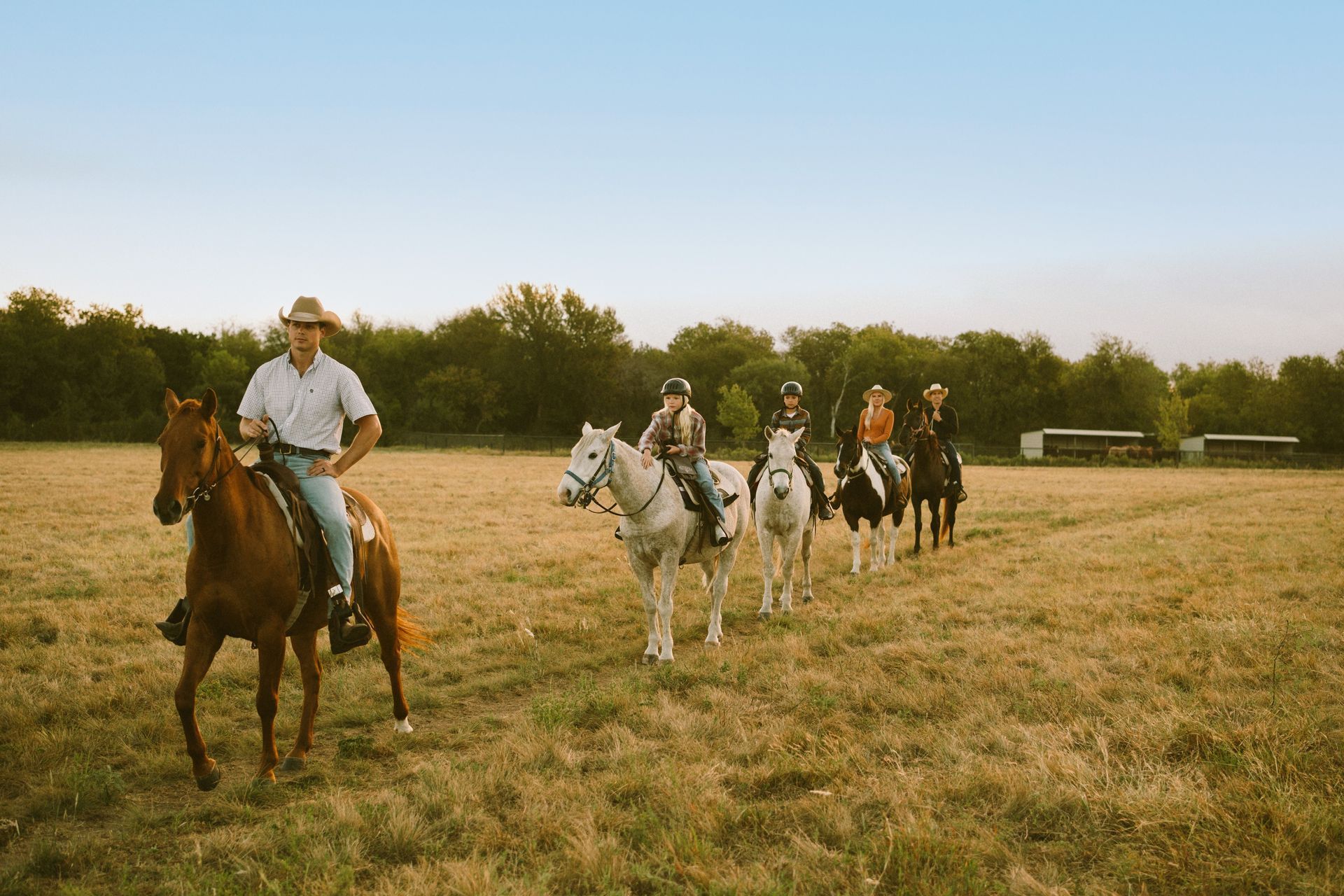 Five people on horseback at sunset overlooking a river.