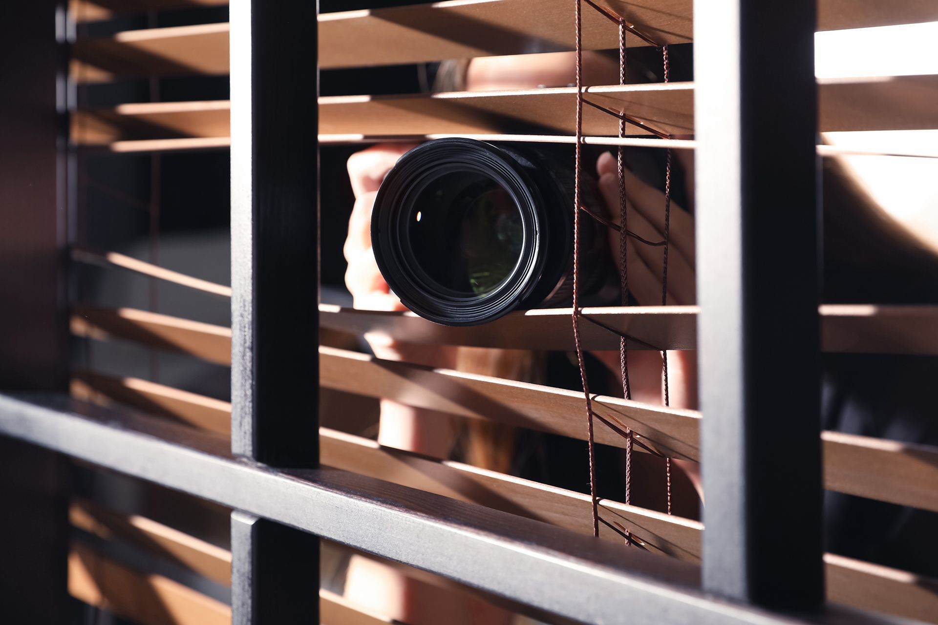 A Person Is Holding a Camera and Looking Through Blinds