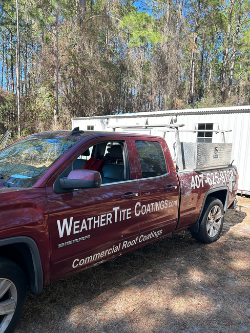 A red WeatherTite Coatings truck is parked in the dirt in front of a trailer.
