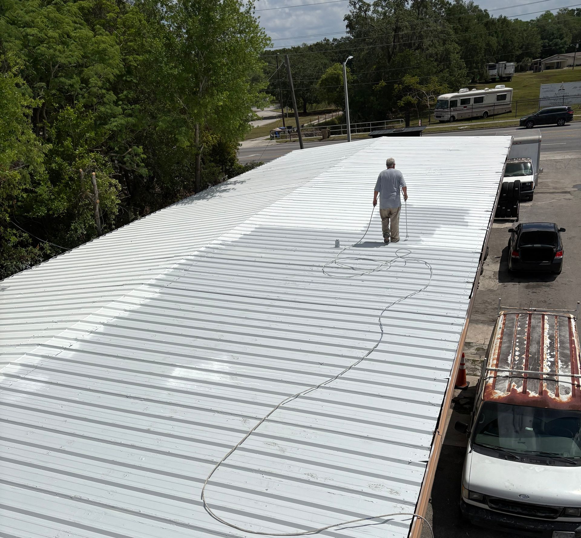 An employee on a commercial building roof is applying roof coating.