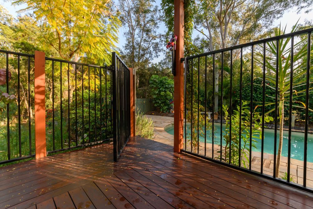 Black metal fence with gate on a wooden deck, leading to a pool in a backyard. — True North Fencing In Noonamah, NT