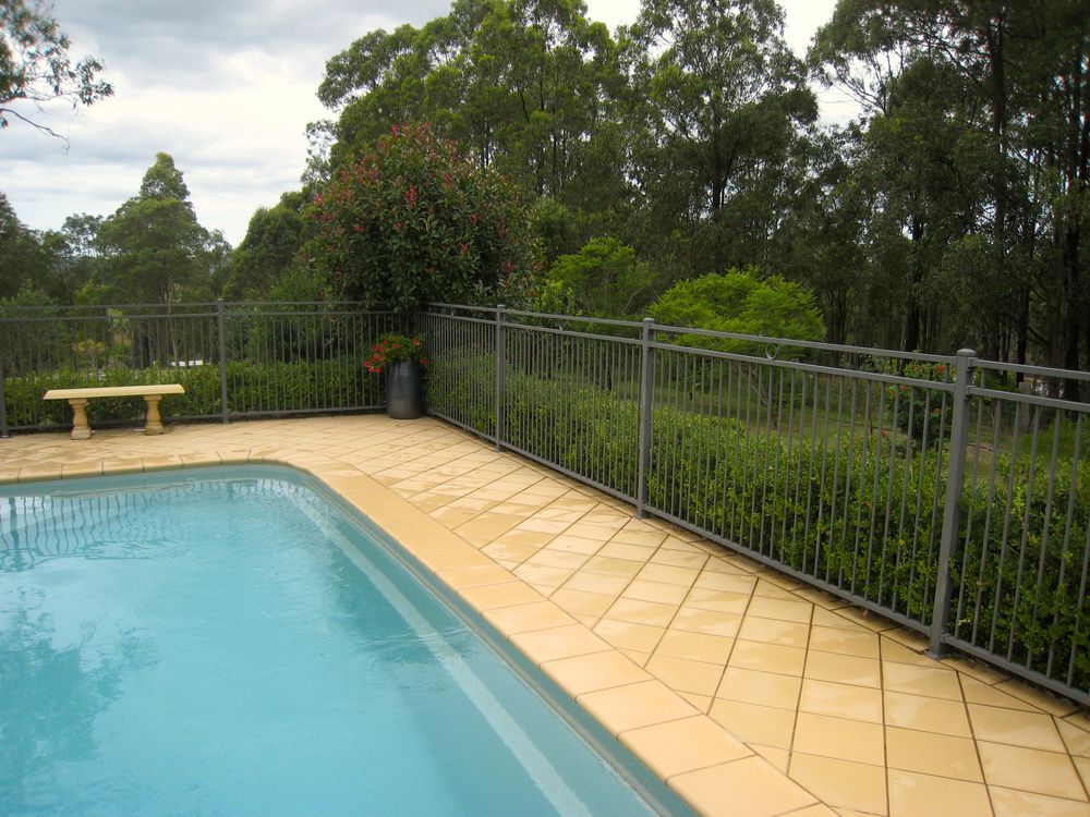 Swimming pool with metal fence and surrounding greenery. Beige tile borders the pool. — True North Fencing In Noonamah, NT