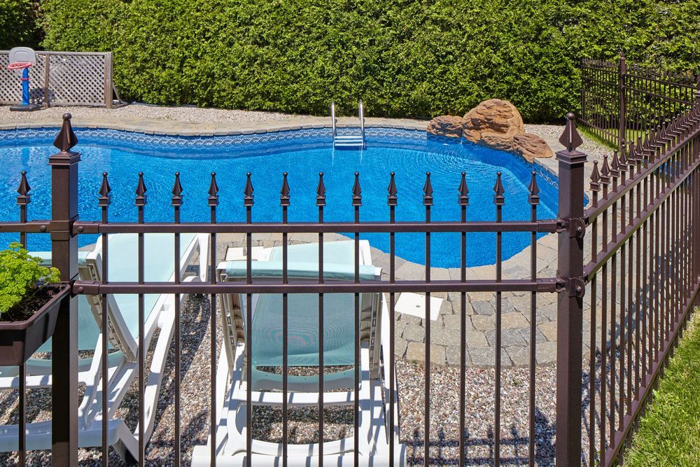 Pool with brown metal fence, surrounded by green foliage, with lounge chairs inside. — True North Fencing In Noonamah, NT