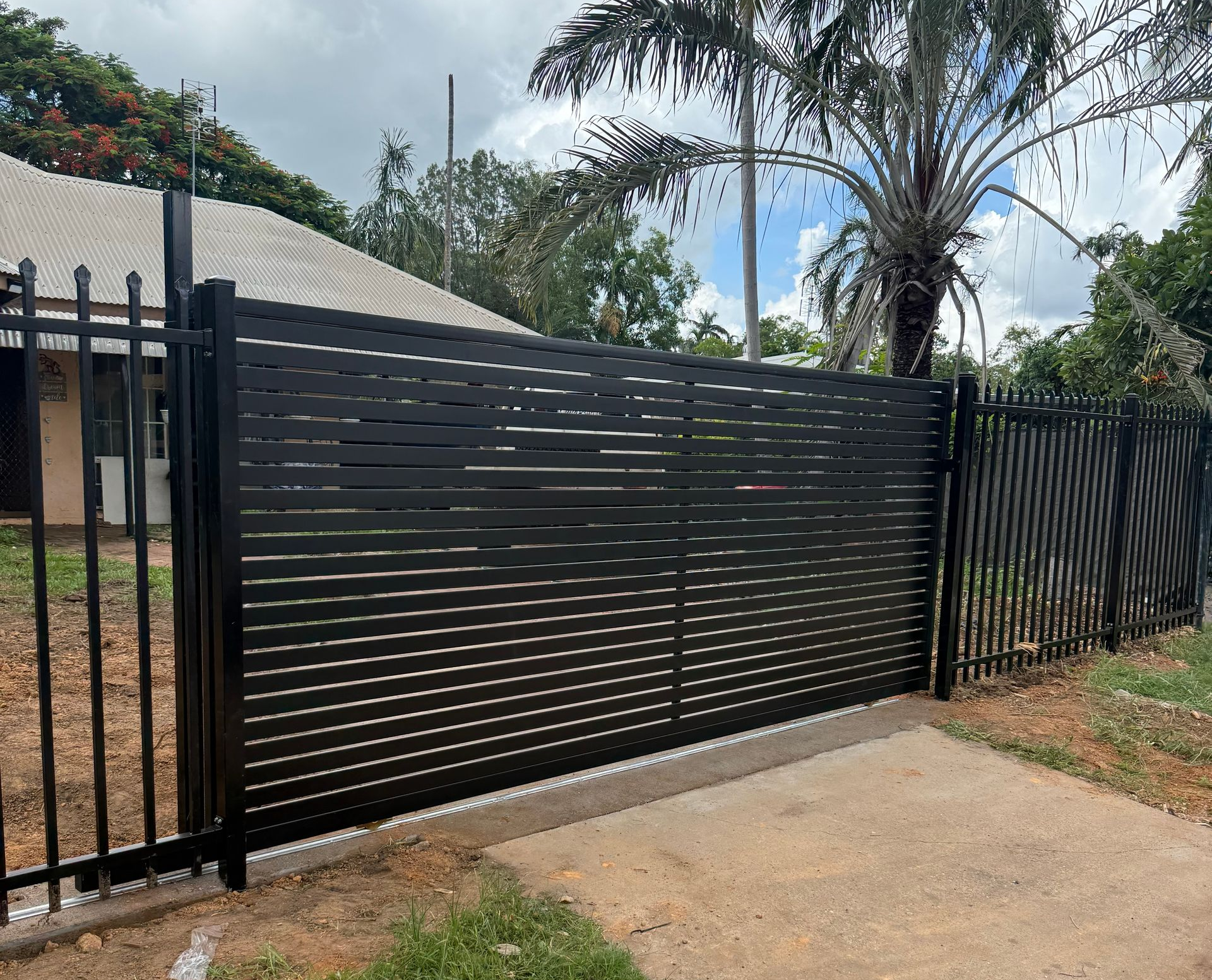 Black metal gate with decorative cutouts, set in a concrete driveway, next to a black fence. — True North Fencing In Noonamah, NT