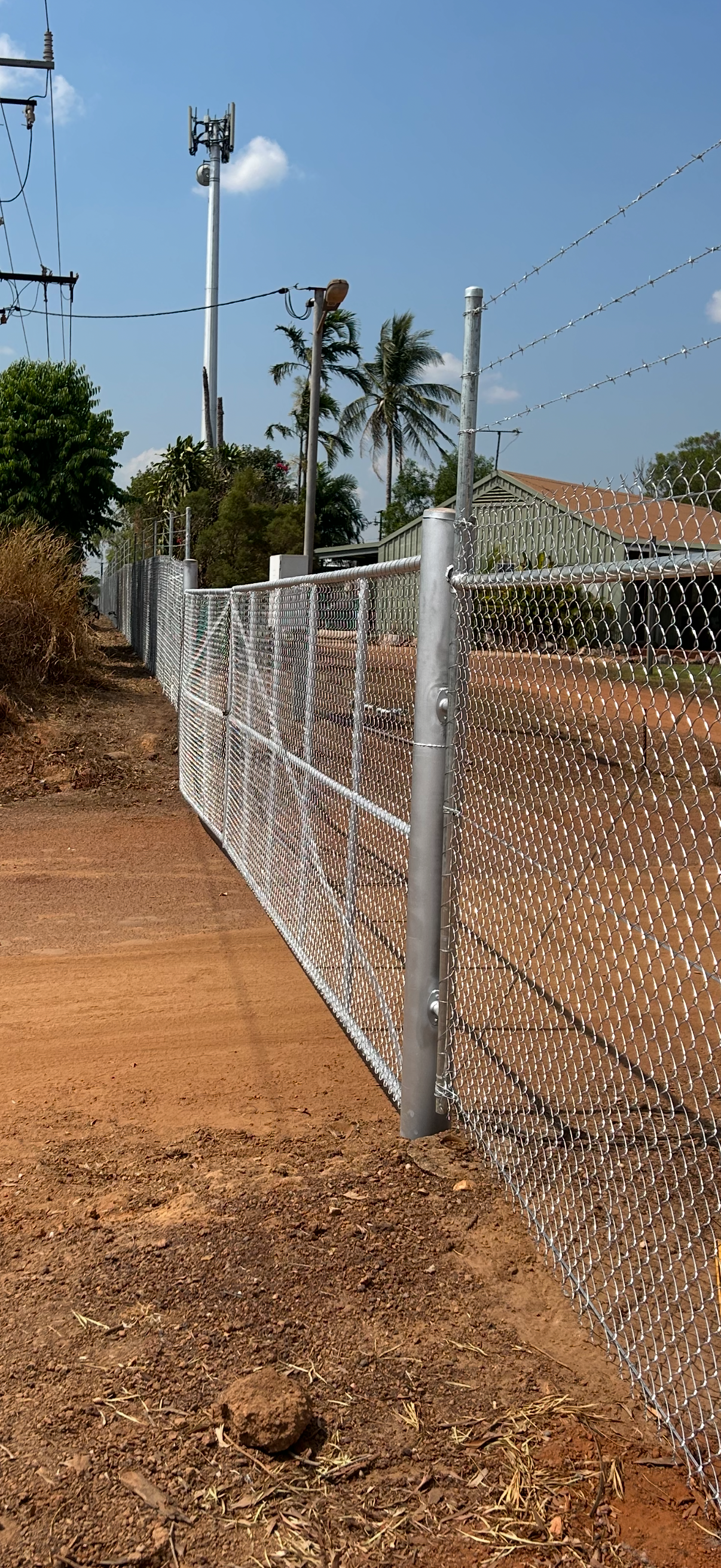 A metal fence with barbed wire runs along a dirt path, with a blue sky in the background. — True North Fencing In Noonamah, NT