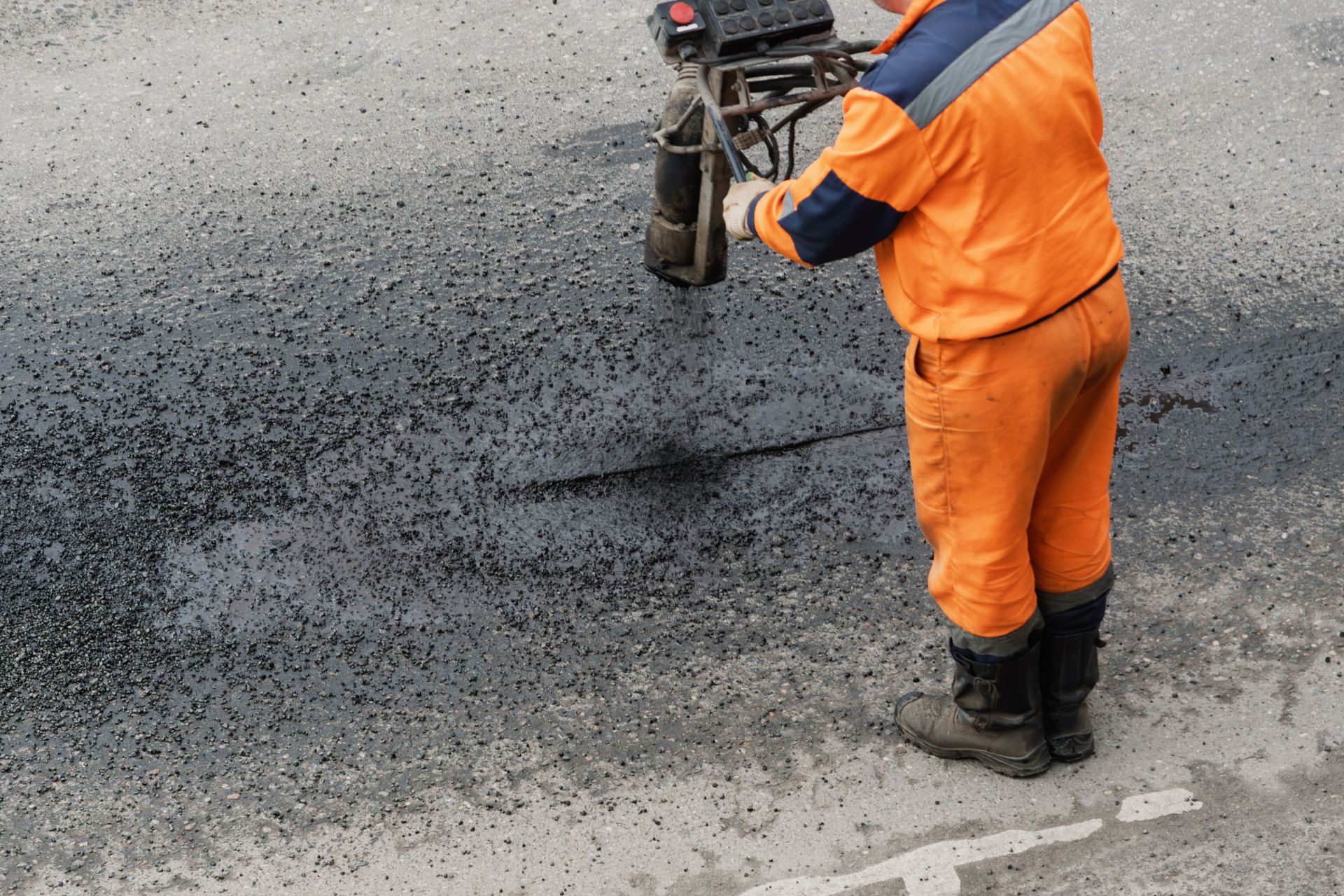 A worker applies hot bitumen to a damaged asphalt seam during pavement repair on a street. A worker applies hot bitumen to a damaged asphalt seam during pavement repair on a street.