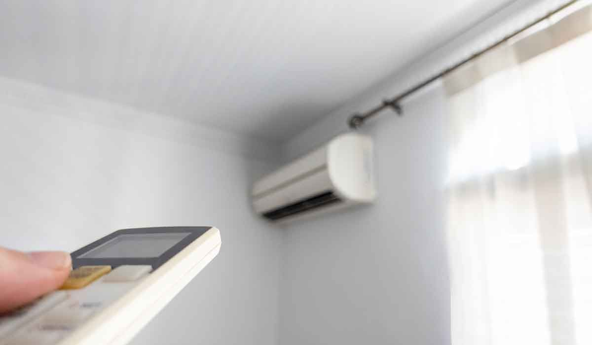 Hand holding remote aimed at a white wall-mounted single-zone mini-split system in Toledo, Ohio