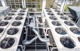 Two rows of industrial rooftop HVAC cooling fans with central metallic piping on a flat roof.