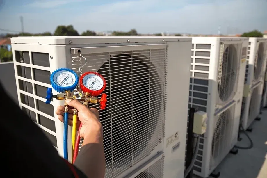 Hand holding HVAC manifold gauges in front of rooftop air conditioning units