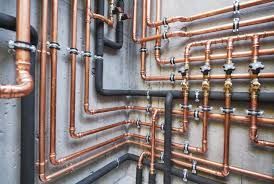 Copper pipes with valves and black foam insulation are mounted neatly against a grey concrete wall.