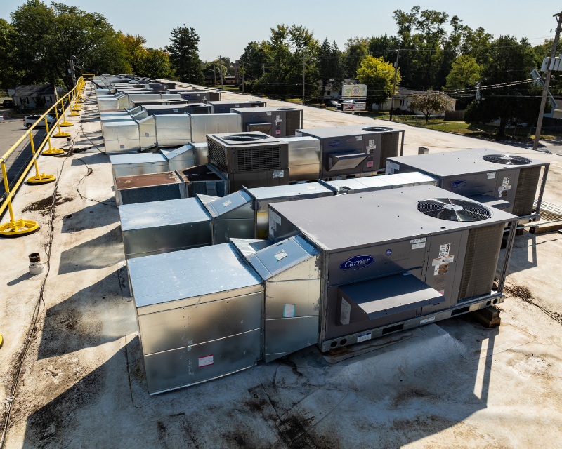 Row of rooftop HVAC units and ducts on a commercial building, viewed from above.