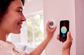 A person adjusting a smart thermostat on a wall while checking the temperature settings on their smartphone.