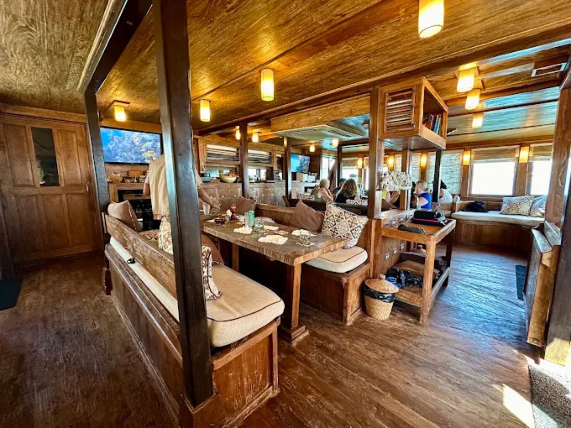 Rustic, wood-paneled boat interior featuring wooden tables, cushioned bench seating, and warm overhead lighting.