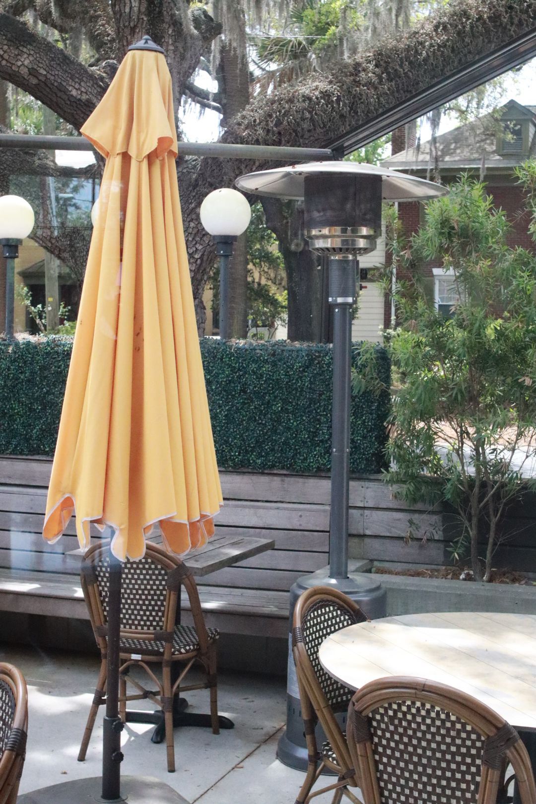 Closed yellow patio umbrella beside outdoor tables and wicker chairs in a shaded courtyard