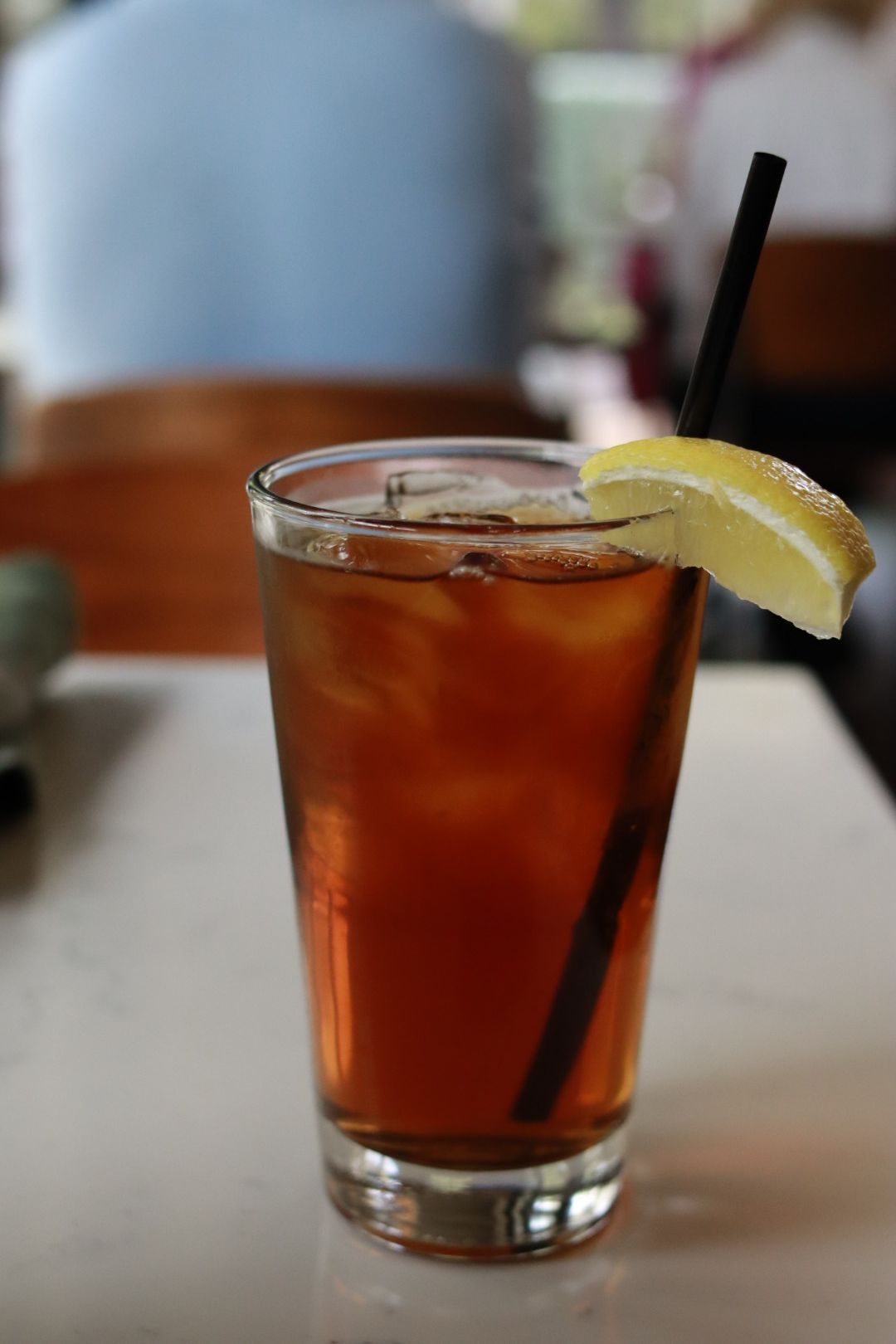 Iced tea in a glass with a lemon wedge and straw on a table
