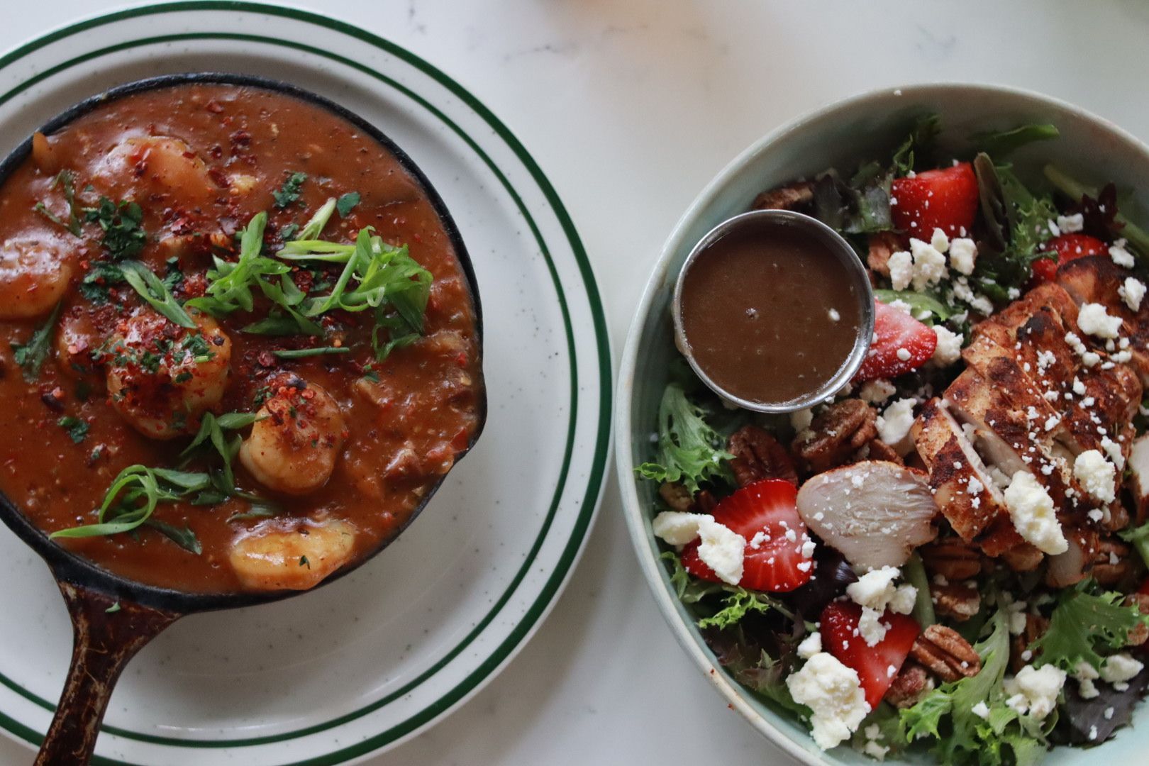 Two bowls of food: a red stew with herbs and a salad with meat and dressing on a white table