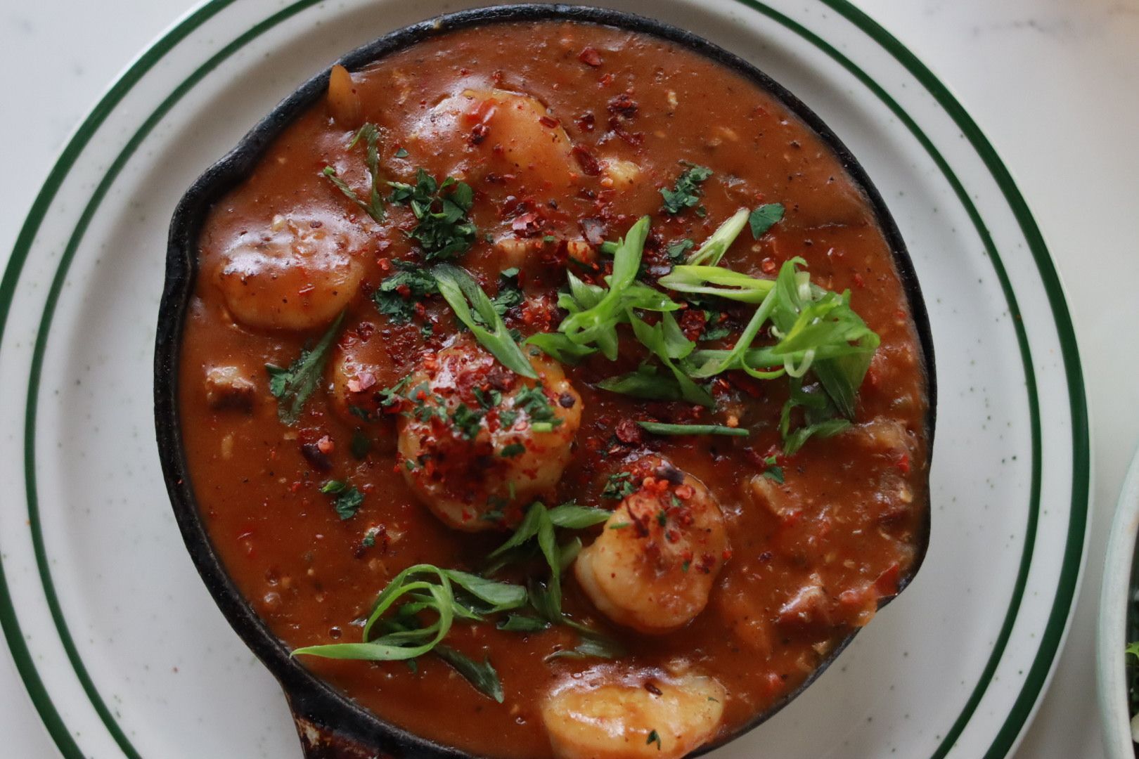 Bowl of red curry with potatoes and herbs, topped with fresh greens on a white plate.